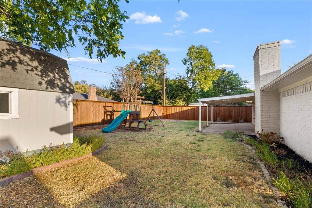 Expansive backyard with a wood privacy fence, separate storage structure, and a covered patio area