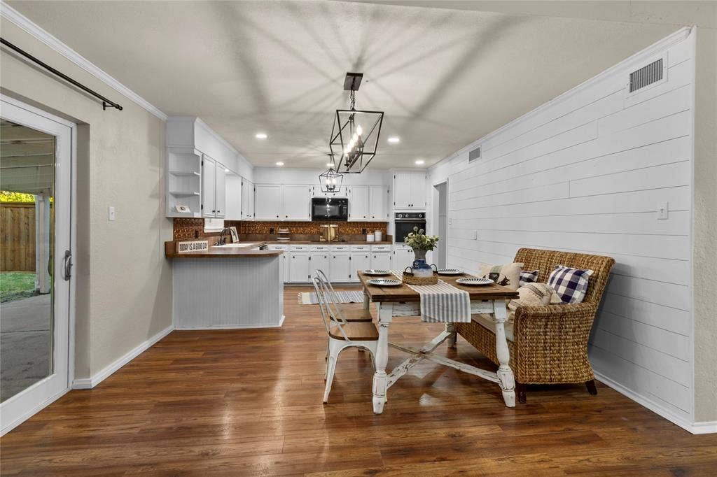 Wood-finish flooring, white cabinetry, dark hardware, integrated appliances, and a linear pendant light fixture