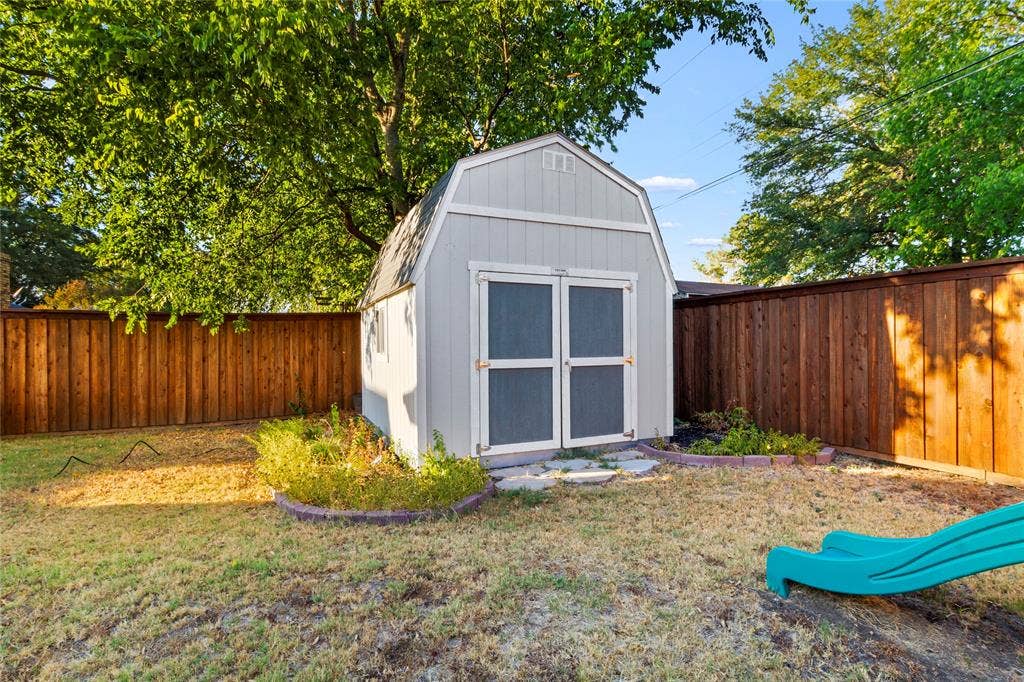 Backyard featuring a shed with double doors, wood fencing, and mature trees