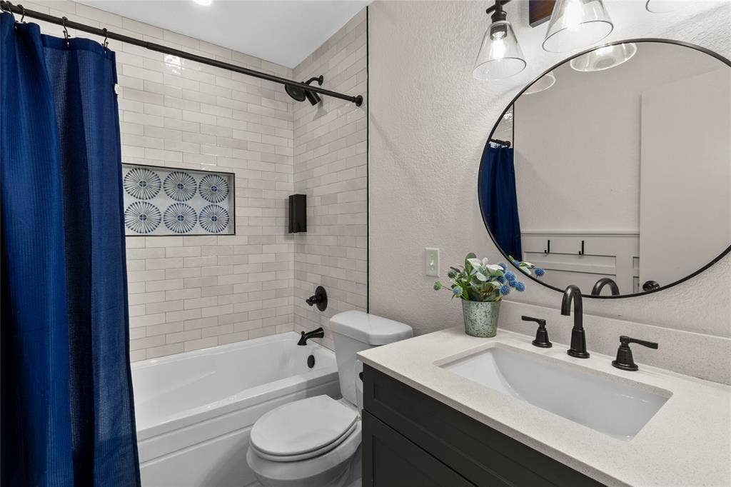 Bathroom featuring white subway tile, a built-in shower niche, a dark wood-finish vanity, a light stone-look countertop, and matte black fixtures