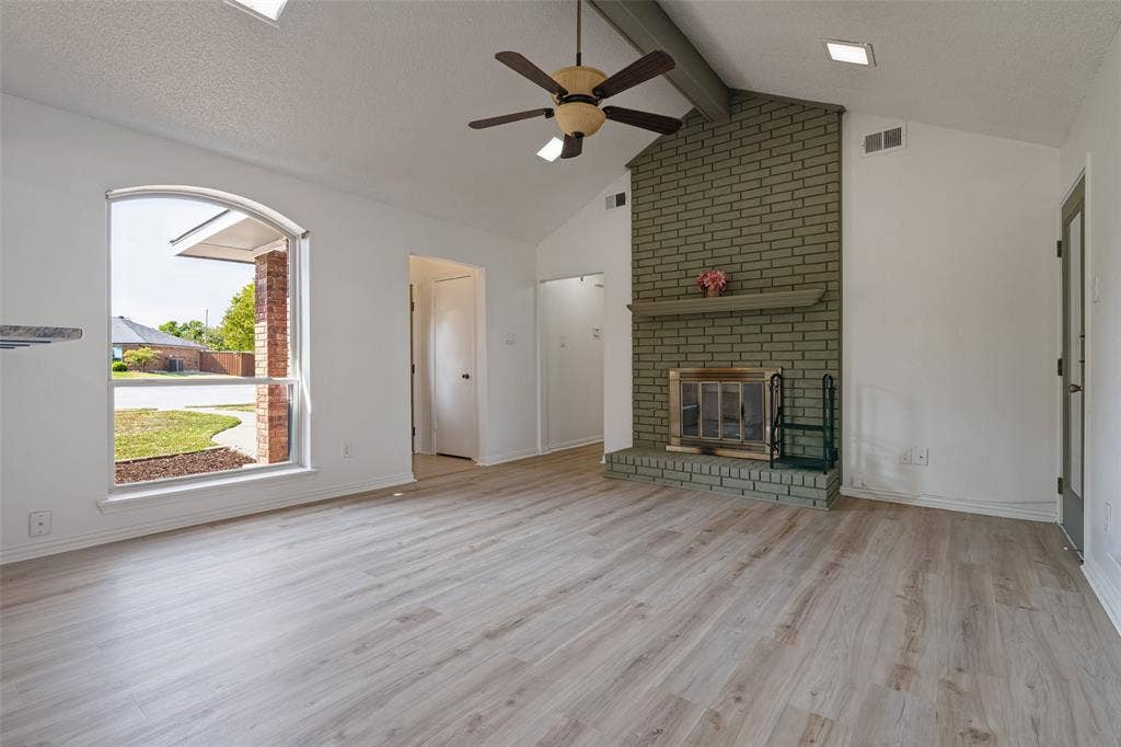 6527 Leasa Court, Sachse, TX 75048 Vaulted ceiling, ceiling fan, brick fireplace, wood-finish flooring, and arched window.