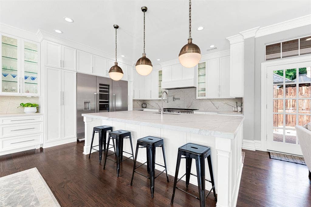 5325 BLAKE Drive, Plano, TX 75093 Crisp white cabinetry paired with quartzite countertops frames a oversized center island with breakfast bar seating. High-end stainless steel Thermador appliances, glass-front upper displays, and chic globe pendant lights complete this bright, contemporary kitchen workspac