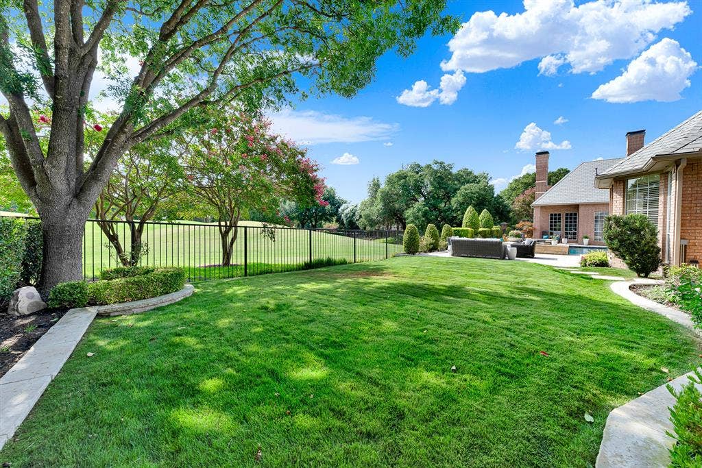 5325 BLAKE Drive, Plano, TX 75093 A manicured green lawn framed by wrought-iron fencing offers unobstructed views of the adjacent golf course fairway. Mature shade trees and stone-paved walkways border the yard, creating a tranquil transition between the private lawn and the rear patio entertaining area.
