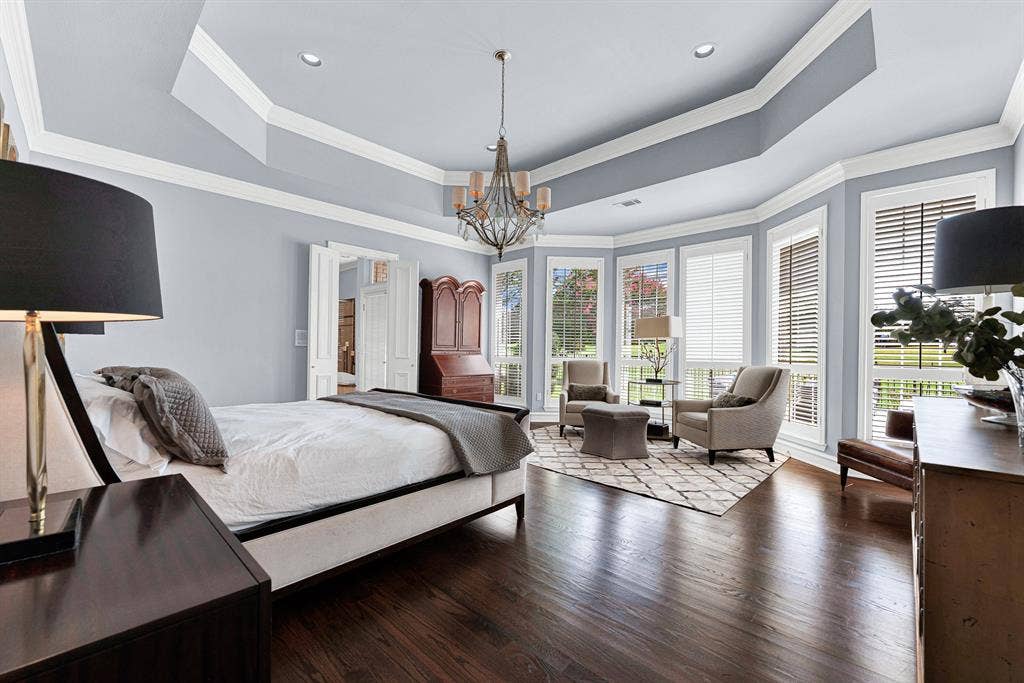 5325 BLAKE Drive, Plano, TX 75093 Rich hardwood floors and an elegant tray ceiling with a rustic chandelier set a sophisticated tone in this expansive primary retreat. A sunlit bay window alcove with plantation shutters easily accommodates a private sitting area overlooking the manicured grounds.