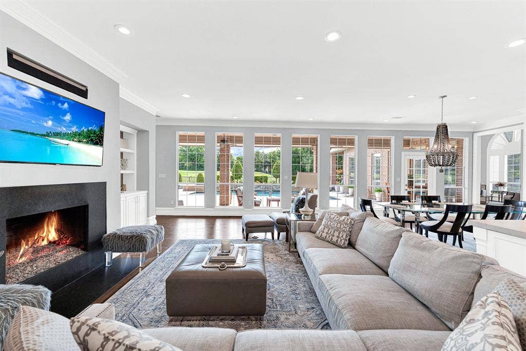 5325 BLAKE Drive, Plano, TX 75093 Expansive floor-to-ceiling windows line the back wall, seamlessly connecting the cozy indoor seating area with the resort-style pool deck outside. The open-concept design flows effortlessly past the modern fireplace directly into the casual dining space and kitchen.