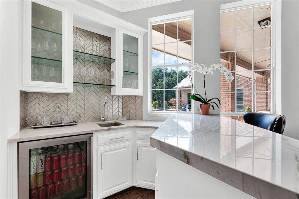 5325 BLAKE Drive, Plano, TX 75093 A stylish herringbone tile backsplash, quartz counters, glass-front upper cabinets, and a built-in beverage fridge make host prep effortless. Complete with a prep sink and stemware display, this wet bar delivers both high functionality and modern luxury.