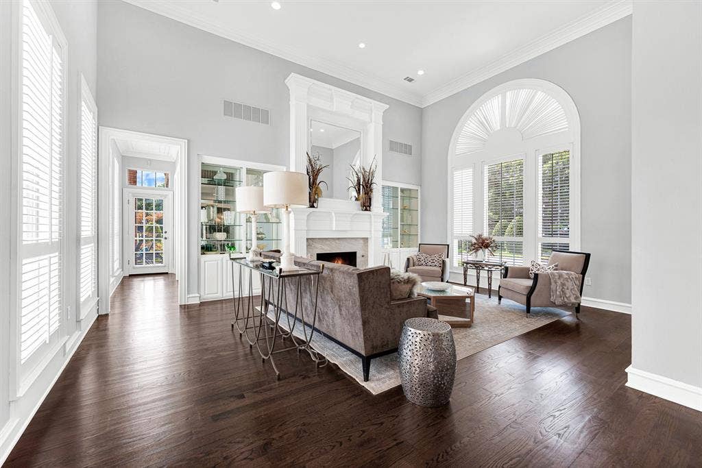 5325 BLAKE Drive, Plano, TX 75093 Soaring ceilings and an elegant fireplace mantle anchor this sunlit formal living space, framed by expansive arched windows and custom built-in display cabinetry. Perfect for entertaining guests, the effortless floor plan naturally flows right into the surrounding main-level living areas.