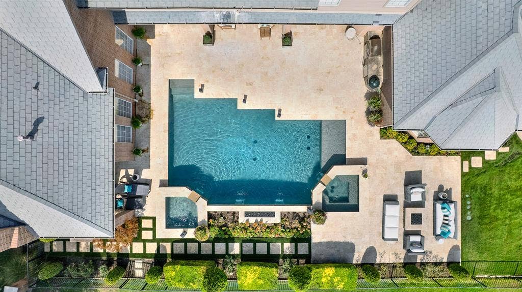 5325 BLAKE Drive, Plano, TX 75093 A straight-down aerial shot highlights the geometric luxury of the swimming pool, dual integrated hot tub, and surrounding travertine decking. Built-in fire features, sunbathing ledges, and landscaped pathways show off the backyard's layout.