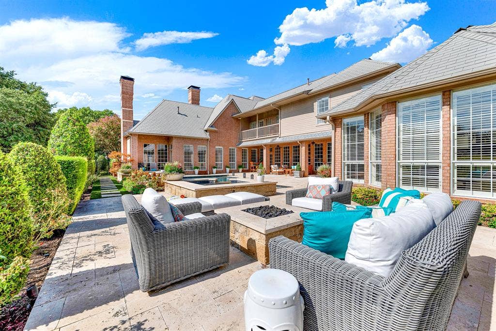 5325 BLAKE Drive, Plano, TX 75093 Travertine pavers create a sprawling rear patio outfitted with an integrated fire pit and cozy wicker lounge seating. The classic brick-and-siding exterior frames this private outdoor sanctuary, complete with views of the pool and lush perimeter landscaping.