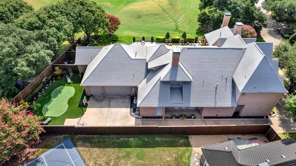 5325 BLAKE Drive, Plano, TX 75093 An elevated top-down view shows the home's multi-tiered slate roofline alongside the garage motor court. You can practice your game on the custom turf putting green sits tucked in the side yard, complemented by landscaping and privacy fencing.
