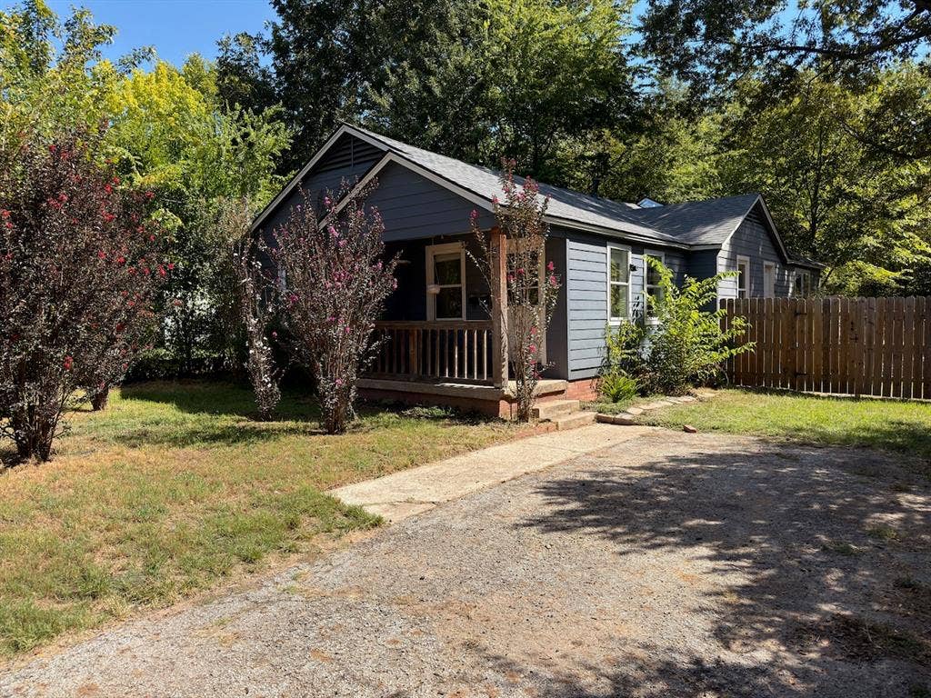 3014 Crestview Street, Tyler, TX 75701 Blue exterior siding, wood fence, front porch with wood railings, gravel driveway, and mature landscaping