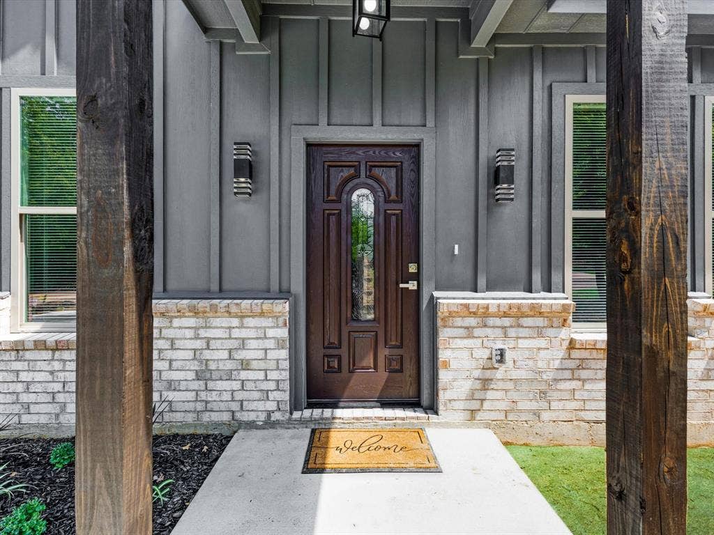 292 Harris Boulevard, Malakoff, TX 75148 Board and batten siding with a brick facade, wood-finish columns, a dark wood-paneled entry door with glass insert, and modern exterior sconces
