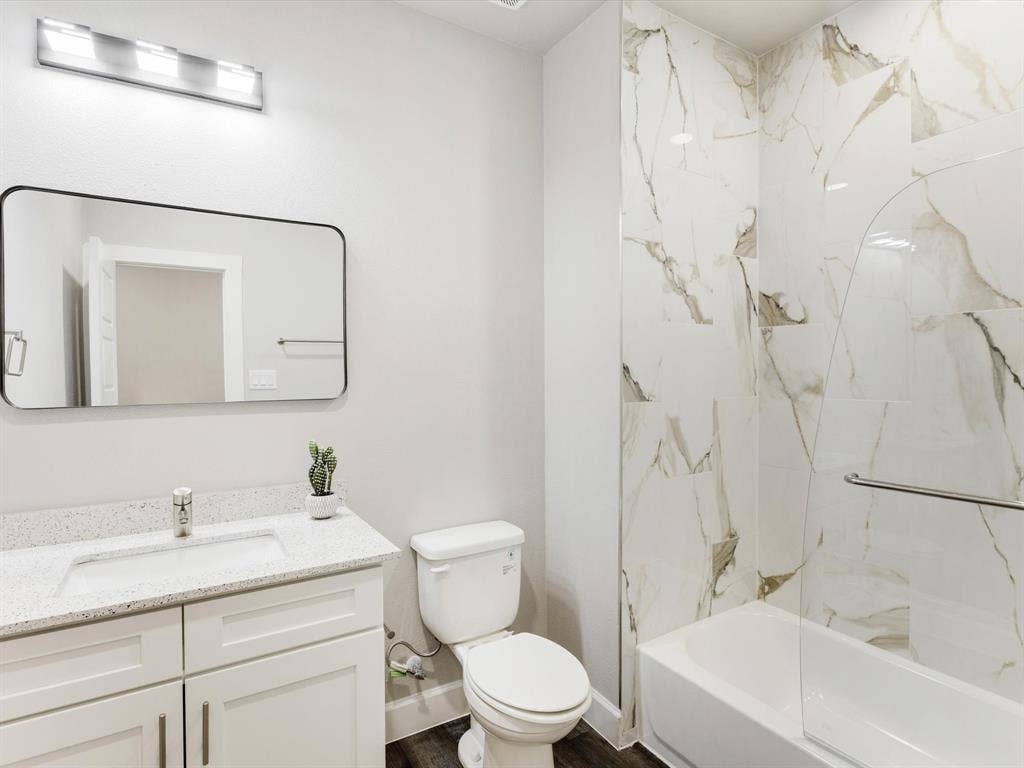 292 Harris Boulevard, Malakoff, TX 75148 White vanity with a speckled countertop and integrated sink, framed mirror, and a tub-shower combination with floor-to-ceiling veined tile surround