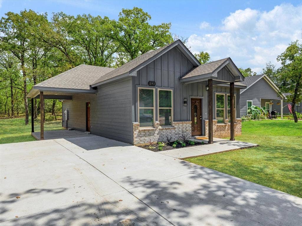 292 Harris Boulevard, Malakoff, TX 75148 Contemporary exterior featuring a covered porch, board and batten siding, stone accents, a wood-finish front door, and an expansive concrete driveway