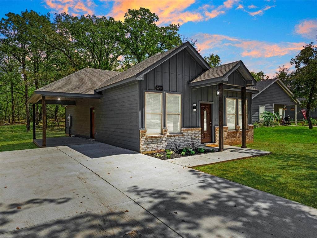 292 Harris Boulevard, Malakoff, TX 75148 Exterior featuring dark gray siding, stone veneer accents, an attached covered carport, a covered front porch with wood-finish columns, and a concrete driveway