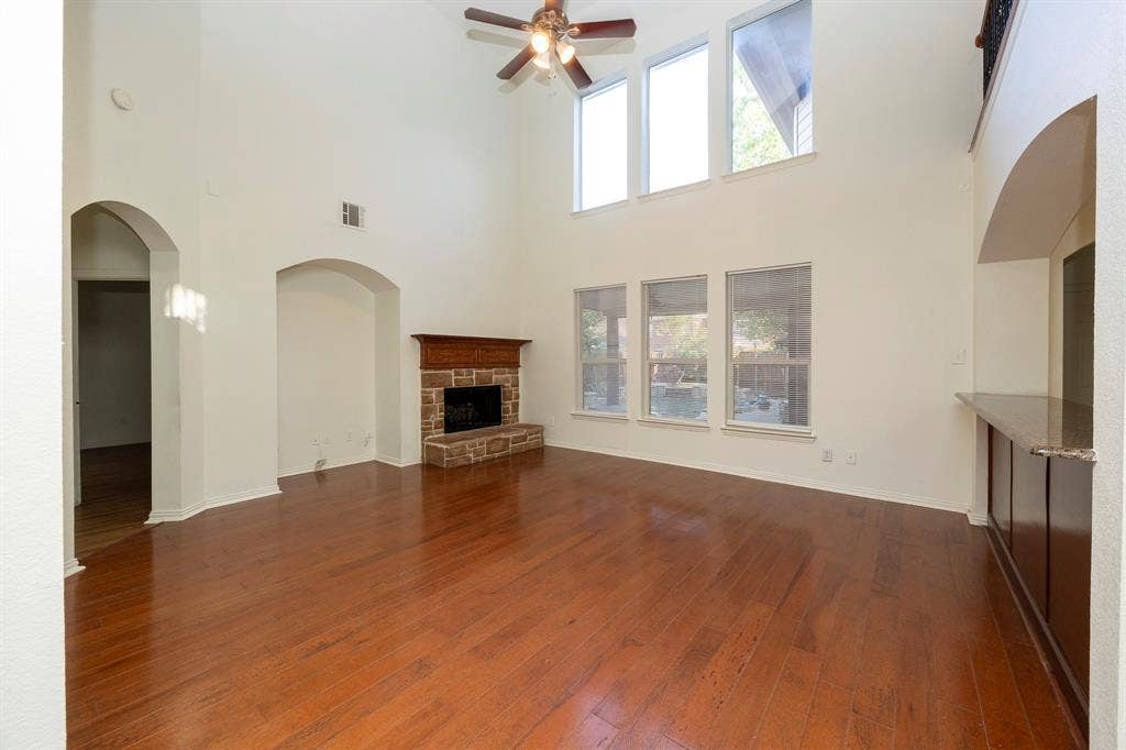 6405 Sapphire Drive, McKinney, TX 75070 Vaulted ceiling with a ceiling fan, stone-faced fireplace with a wood mantle, wood-finish flooring, and multiple windows