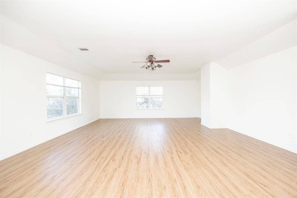 6405 Sapphire Drive, McKinney, TX 75070 Expansive interior featuring wood-finish flooring, white walls, multiple windows, and a ceiling fan