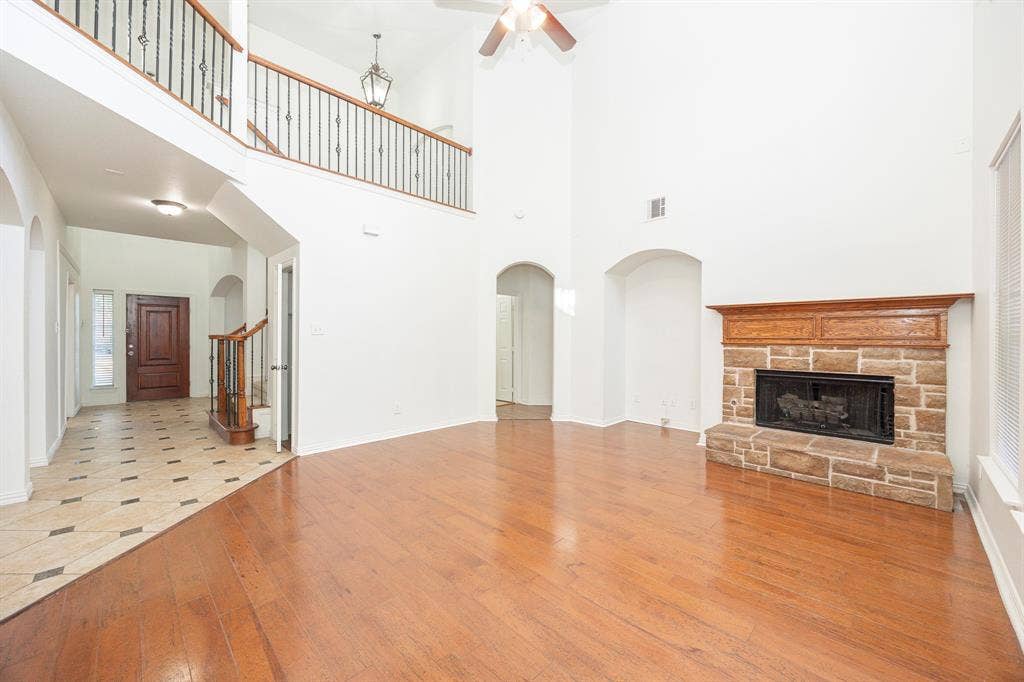 6405 Sapphire Drive, McKinney, TX 75070 Two-story living area with hardwood flooring, a stone-surround fireplace with wood mantel, and an upper-level balcony with wrought iron railing