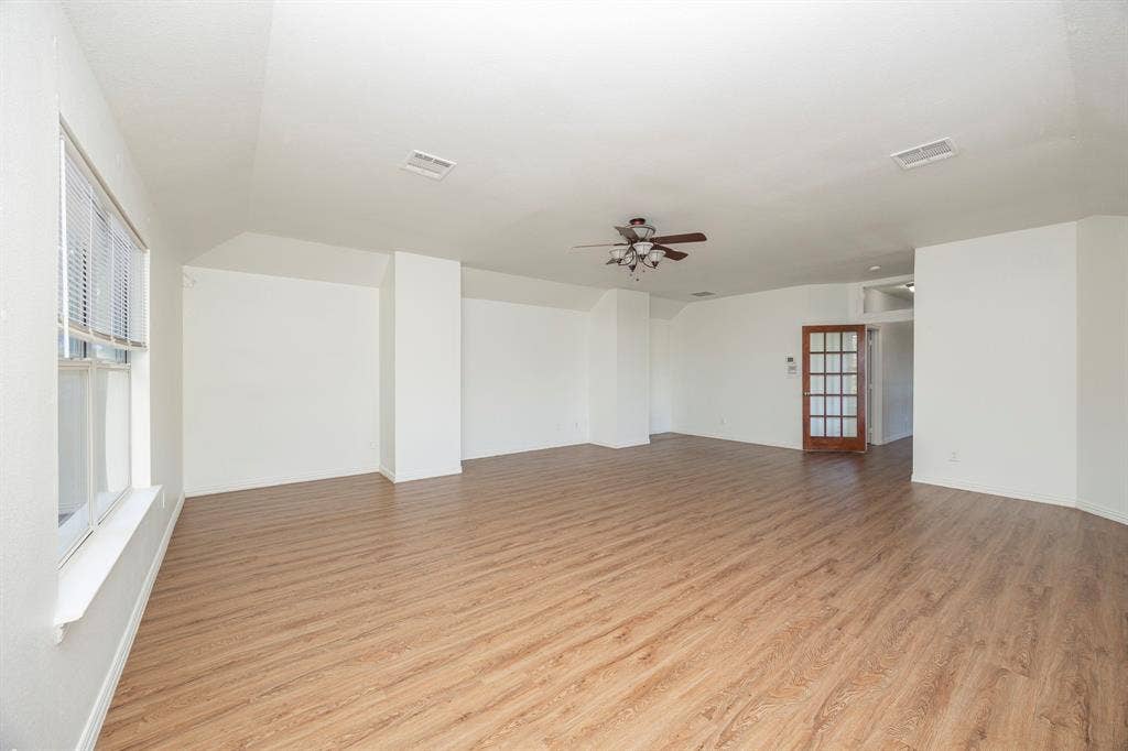 6405 Sapphire Drive, McKinney, TX 75070 Expansive room featuring wood-finish flooring, multiple windows with blinds, a ceiling fan, and a wood-paneled door with glass inserts