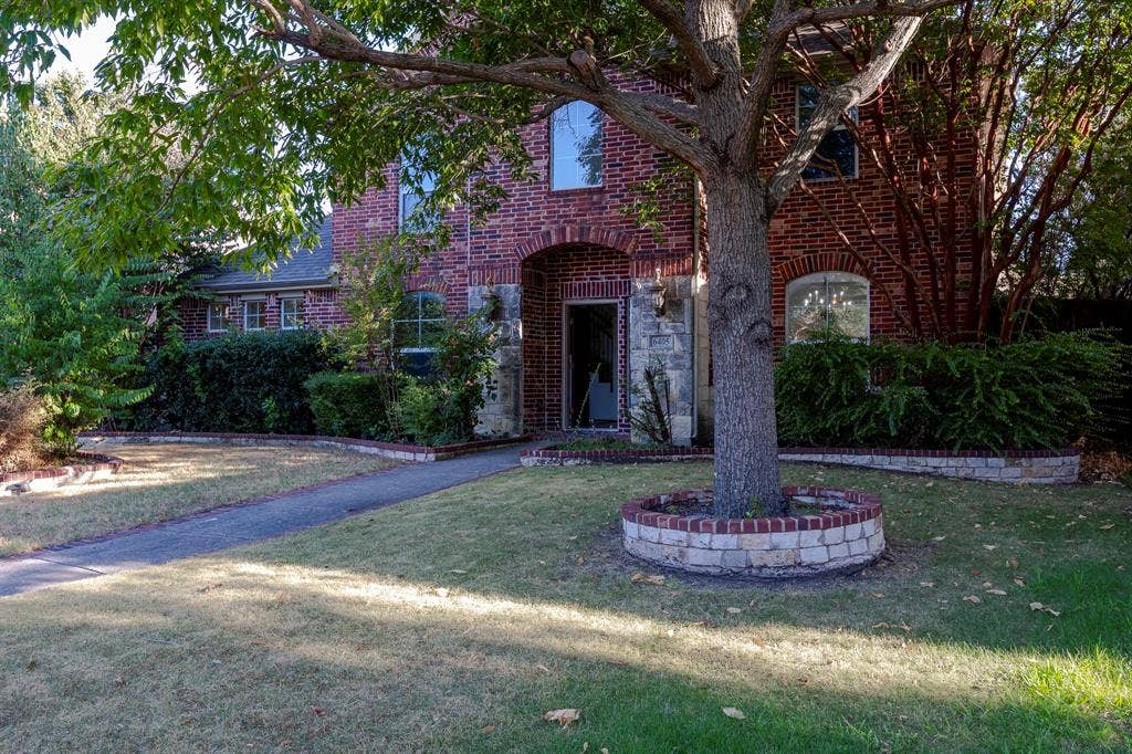 6405 Sapphire Drive, McKinney, TX 75070 Brick exterior with stone accents, arched entryway, mature front yard tree with brick and stone surround, and established landscaping