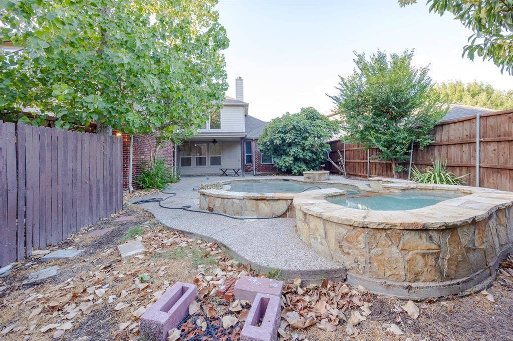 6405 Sapphire Drive, McKinney, TX 75070 Backyard featuring a multi-tiered stone-clad spa, an expansive concrete patio, and mature perimeter trees