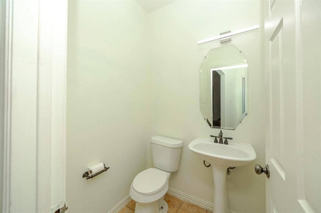 6405 Sapphire Drive, McKinney, TX 75070 Pedestal sink with dark-toned fixtures, an octagonal mirror, and a wall-mounted light fixture
