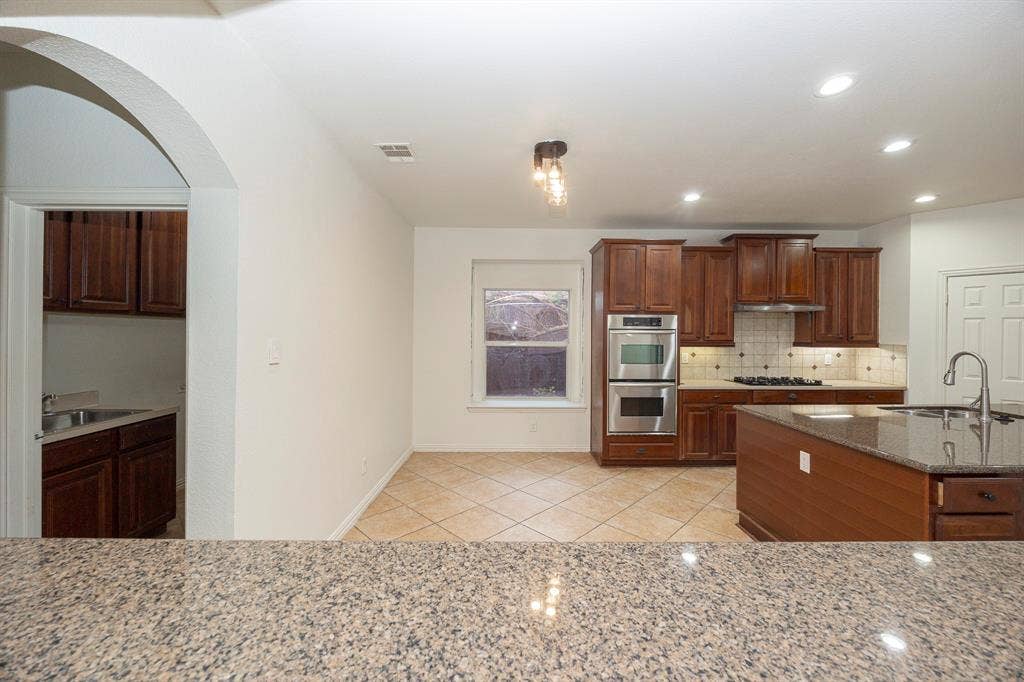 6405 Sapphire Drive, McKinney, TX 75070 Kitchen featuring dark wood cabinetry, stainless steel double wall ovens, a center island with sink, and tile flooring