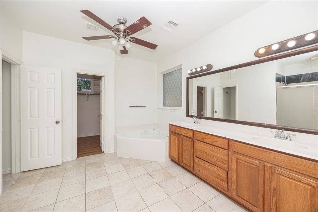 6405 Sapphire Drive, McKinney, TX 75070 Dual vanity with wood-finish cabinetry, a large built-in mirror, and overhead lighting