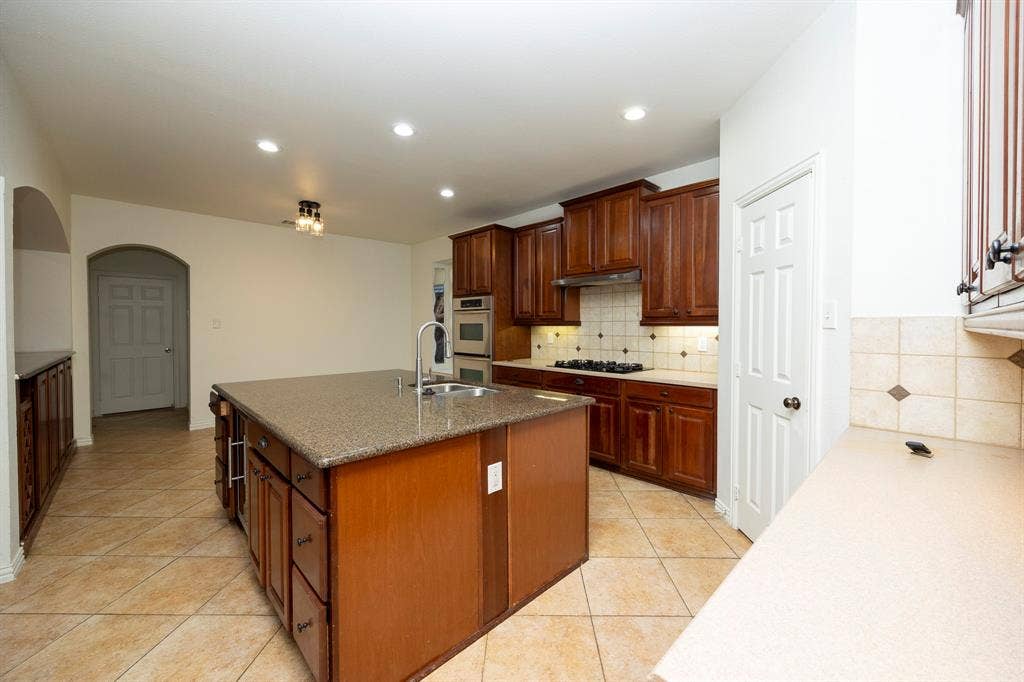 6405 Sapphire Drive, McKinney, TX 75070 Spacious kitchen featuring a large central island, dark wood cabinetry, integrated stainless steel appliances, and tile flooring