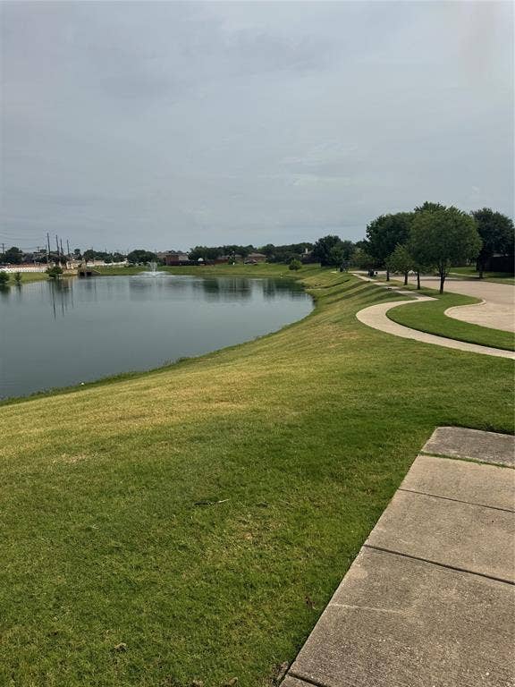 Expansive waterfront with a fountain feature, surrounded by a curving concrete pathway and lush green landscaping