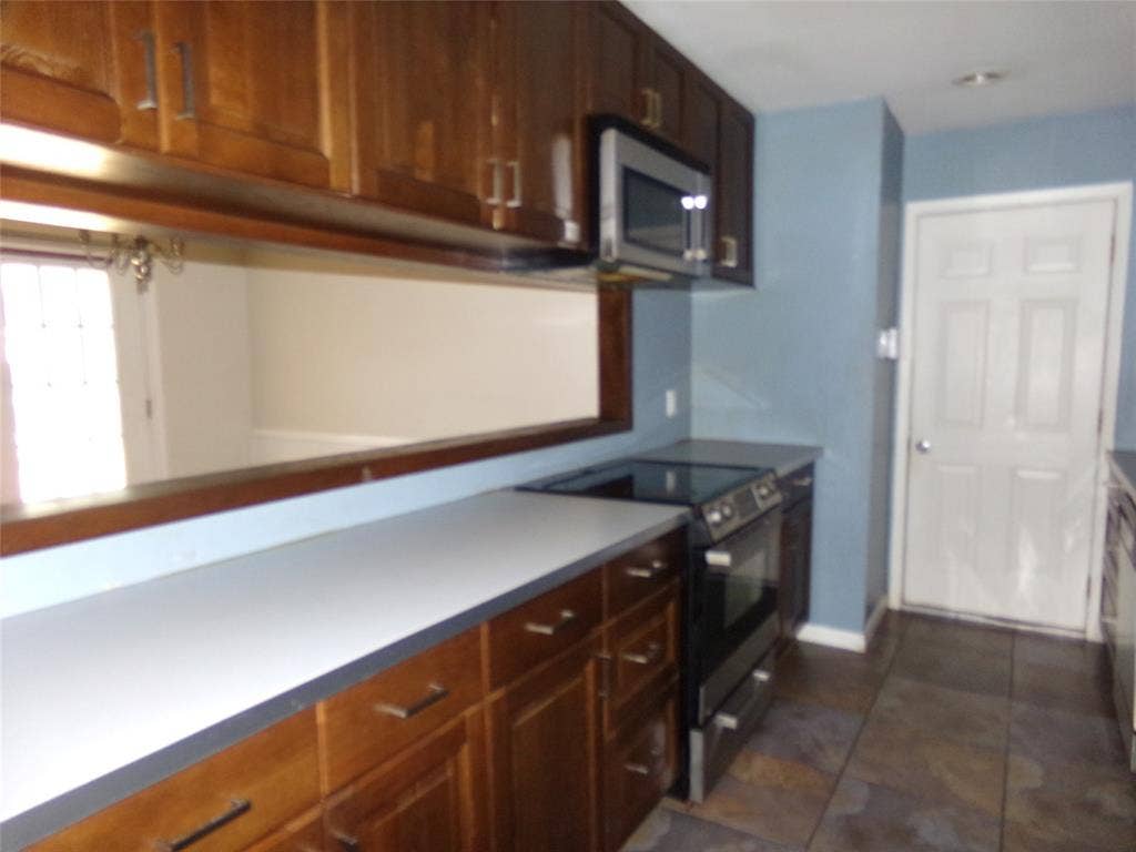 211 S Alexander Avenue, Duncanville, TX 75116 Wood-finish cabinetry with modern hardware, integrated stainless steel microwave, black electric range, and stone tile flooring