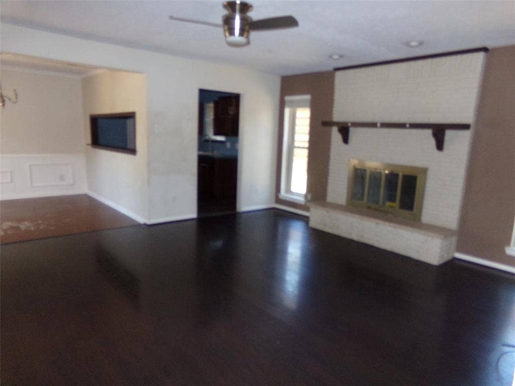 211 S Alexander Avenue, Duncanville, TX 75116 Dark wood-finish flooring, white brick fireplace with a hearth, pass-through window, and a ceiling fan