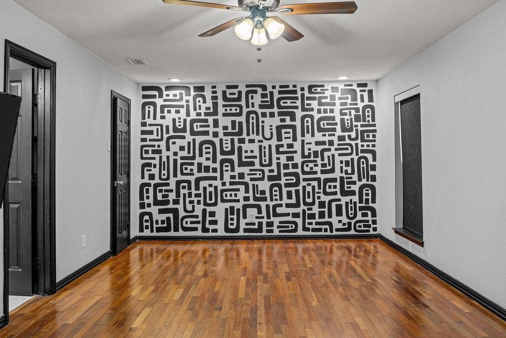9302 Chimney Sweep Lane, Dallas, TX 75243 Wood-finish flooring, a decorative accent wall, a ceiling fan with integrated lighting, and dark trim details