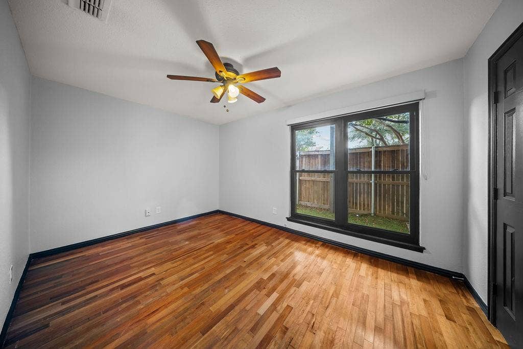 9302 Chimney Sweep Lane, Dallas, TX 75243 Wood-finish flooring, ceiling fan with integrated lighting, window with black trim, white walls, and a paneled door
