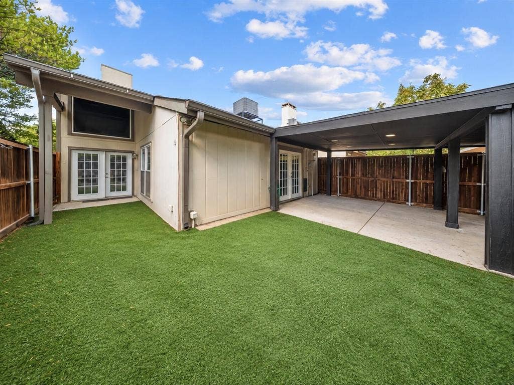 9302 Chimney Sweep Lane, Dallas, TX 75243 Expansive artificial turf backyard with a covered patio, French doors, and a detached carport
