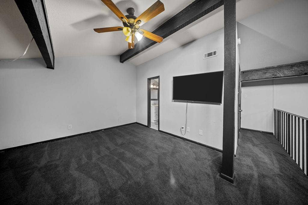 9302 Chimney Sweep Lane, Dallas, TX 75243 Vaulted ceiling with exposed beams, wood-finish ceiling fan, wall-mounted television, and dark carpeting
