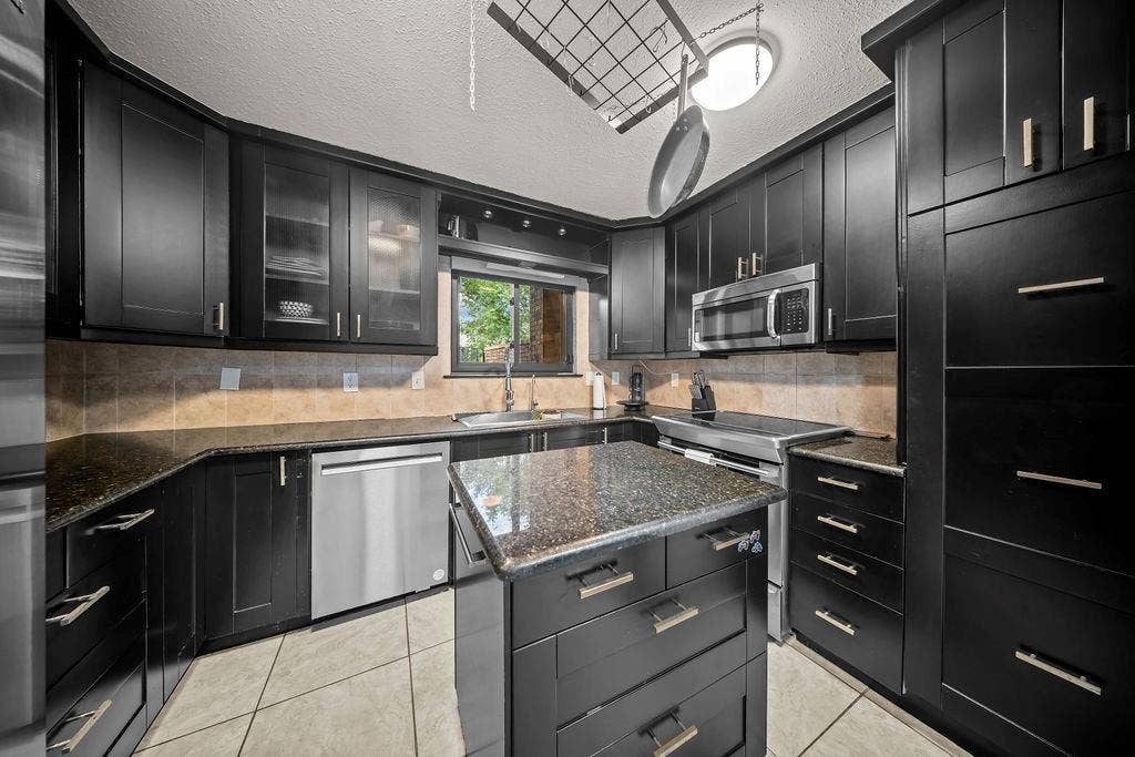 9302 Chimney Sweep Lane, Dallas, TX 75243 Black cabinetry with brushed nickel hardware, granite countertops, stainless steel appliances, and a tiled backsplash