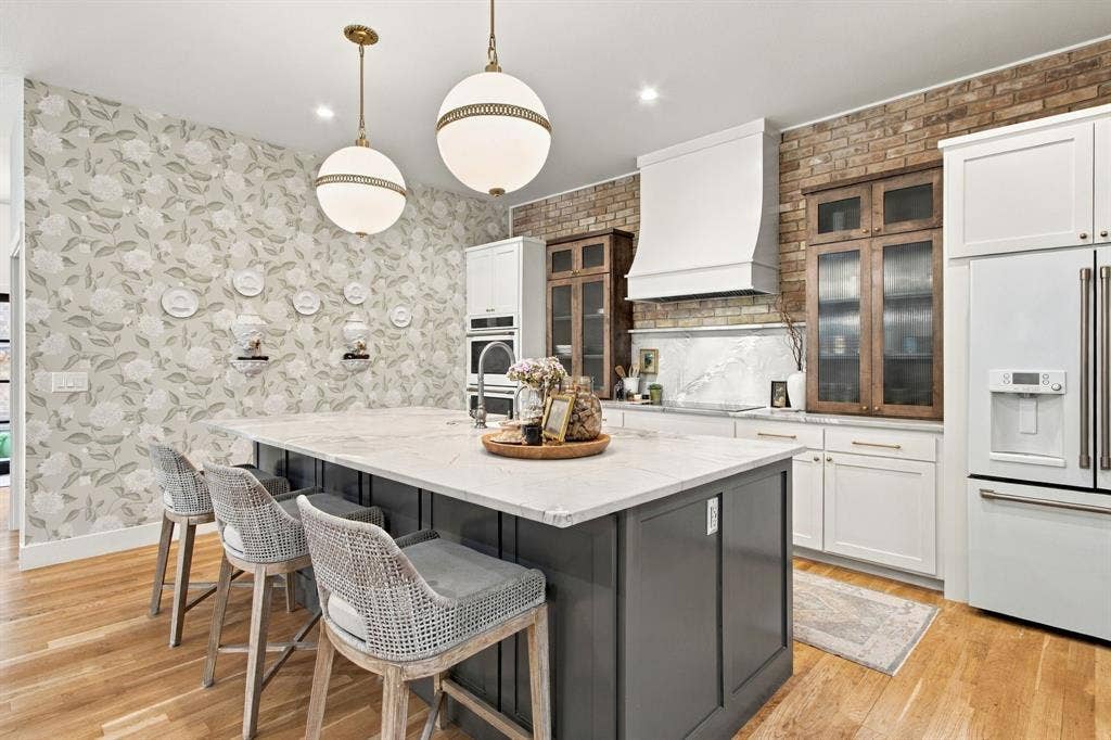 46 Crown Place, Richardson, TX 75080 Spacious kitchen island with a light-toned countertop, wood-finish flooring, two spherical pendant lights, exposed brick accent wall, and integrated stainless steel appliances