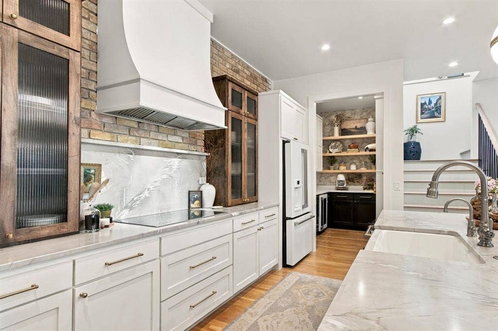 46 Crown Place, Richardson, TX 75080 White shaker cabinetry with brushed brass hardware, brick backsplash, integrated range hood, under-counter beverage refrigerator, and a built-in kitchen sink