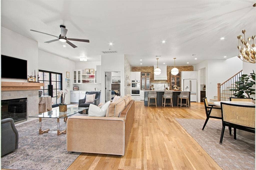 46 Crown Place, Richardson, TX 75080 Hardwood flooring throughout, a modern fireplace with a wood mantel, a kitchen island with pendant lighting, a built-in dry bar with upper glass cabinetry, and a staircase with wood newel posts and railings