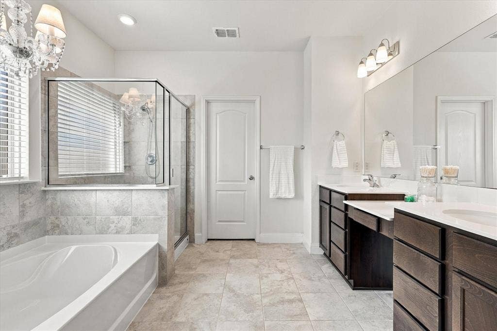 Primary bathroom with shower, dual vanities, and garden tub featuring a chandelier above.