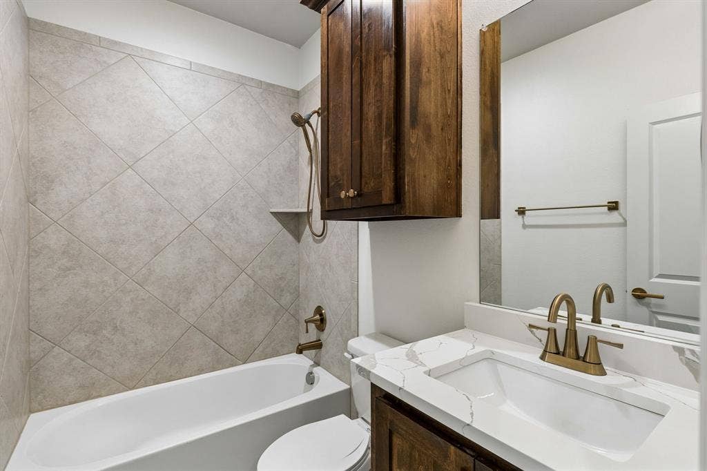 2221 Tremont Boulevard, McKinney, TX 75071 Bathroom featuring a white tub, diagonal tile surround, built-in shower shelf, a vanity with updated quartz countertop, and dark wood-finish cabinet