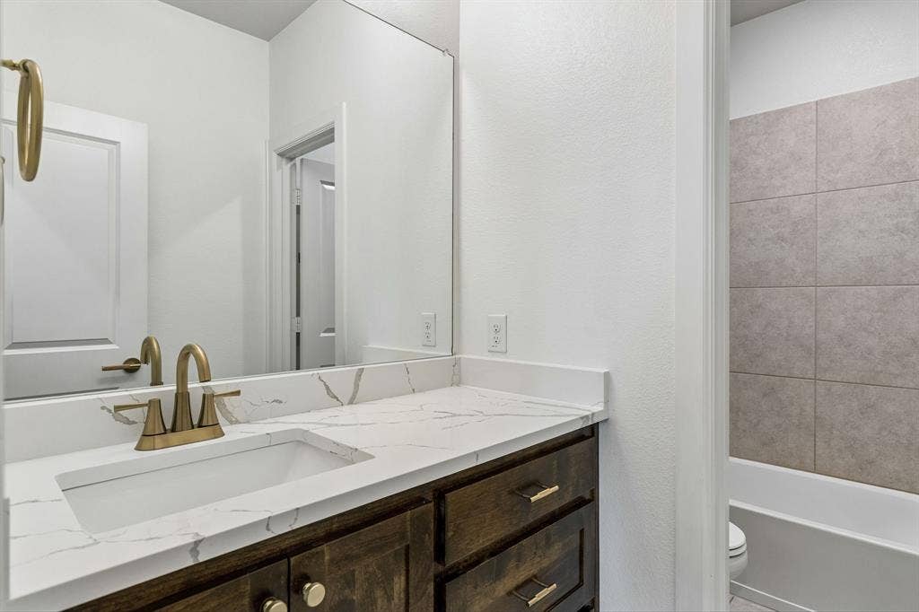 2221 Tremont Boulevard, McKinney, TX 75071 White vanity with a quartz countertop, integrated rectangular sink, and champagne bronze-finish fixtures