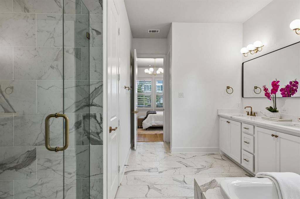 2221 Tremont Boulevard, McKinney, TX 75071 Spacious bathroom featuring a frameless glass shower enclosure, a dual quartz vanity with white cabinetry, a large rectangular mirror, and marble-look tile flooring