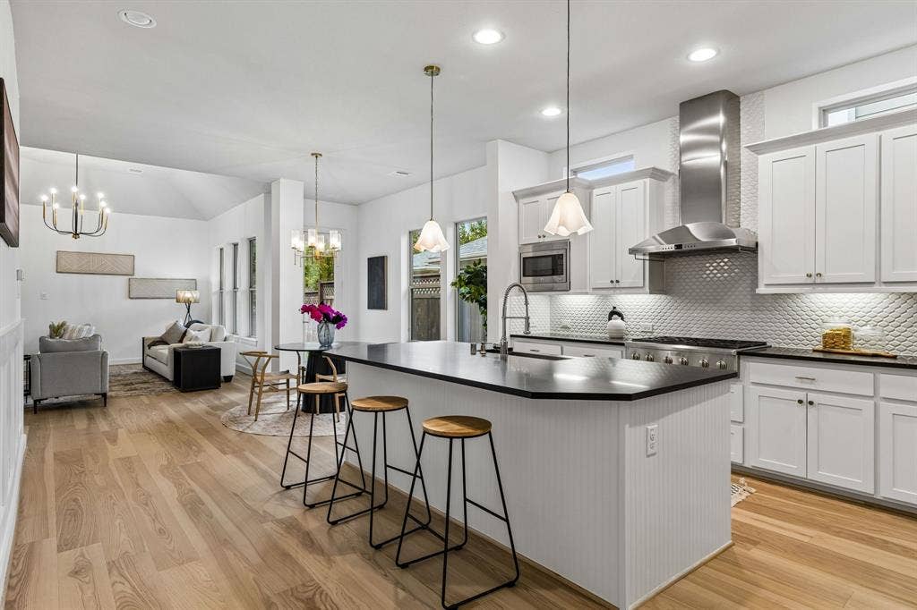 2221 Tremont Boulevard, McKinney, TX 75071 Open-concept layout with white oak hardwood flooring, a kitchen island, white cabinetry, and stainless steel appliances