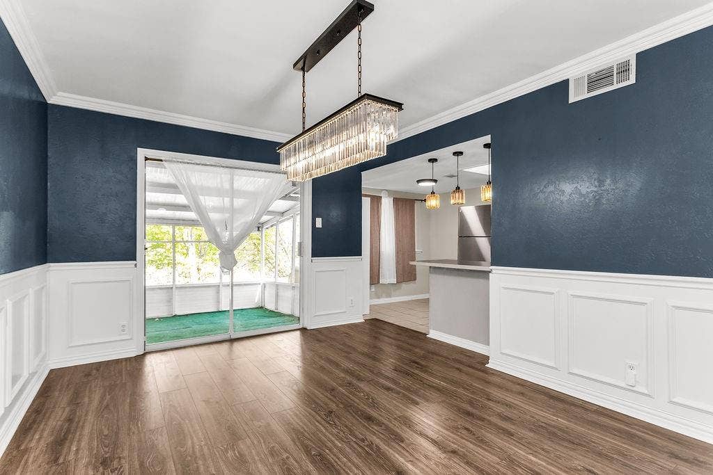 2914 Harvard Street N, Irving, TX 75062 Wood-finish flooring, wainscoting, crown molding, a modern linear chandelier, and sliding glass doors to a screened enclosure