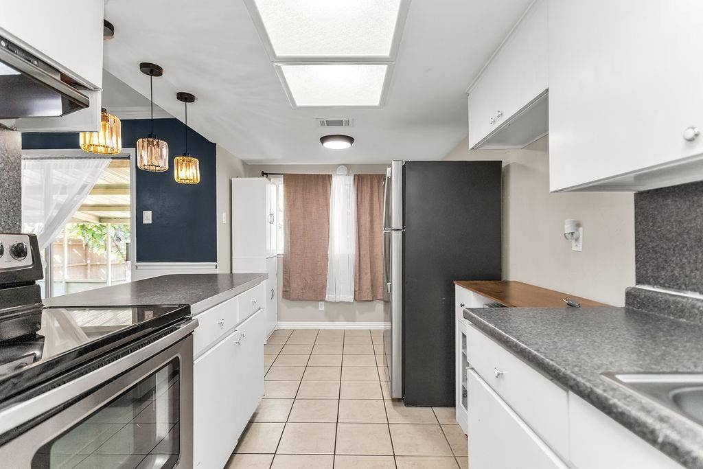 2914 Harvard Street N, Irving, TX 75062 Galley kitchen featuring white cabinetry, dark speckled countertops, tile flooring, and stainless steel appliances