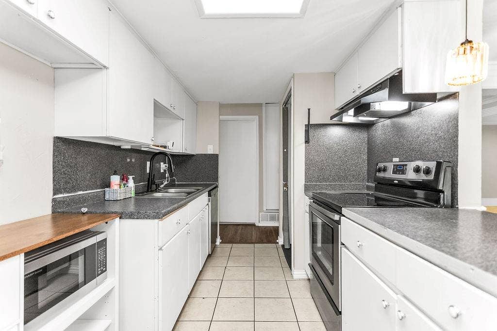 2914 Harvard Street N, Irving, TX 75062 Galley kitchen featuring white cabinetry, dark speckled countertops, a stainless steel double basin sink with a black faucet, and a built-in electric range with an overhead vent hood