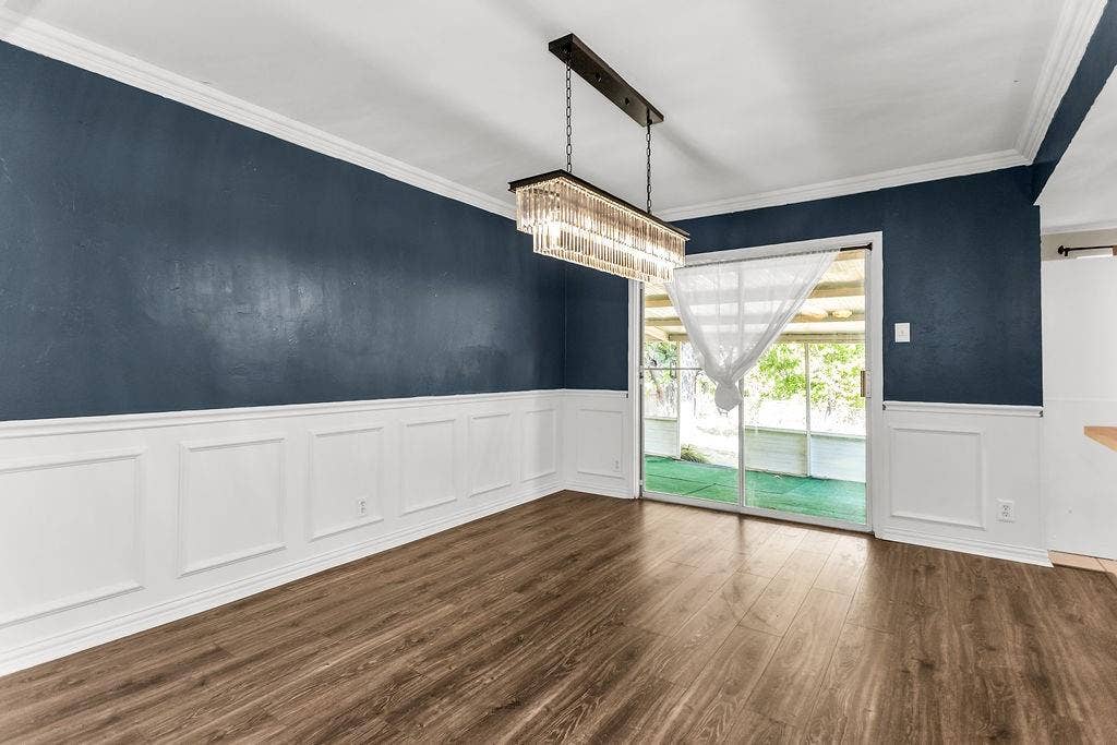 2914 Harvard Street N, Irving, TX 75062 Wood-finish flooring, wainscoting, crown molding, a modern linear chandelier, and sliding glass doors