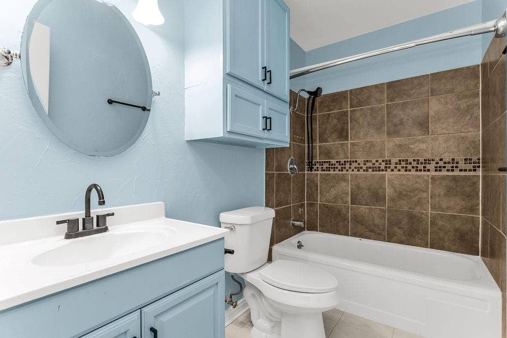 2914 Harvard Street N, Irving, TX 75062 Bathroom featuring a vanity with an integrated sink, blue cabinetry, a wall-mounted mirror, a tub with a shower, and tiled shower walls
